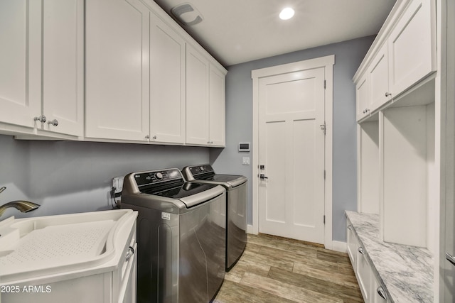 clothes washing area with sink, cabinets, washing machine and clothes dryer, and light hardwood / wood-style floors