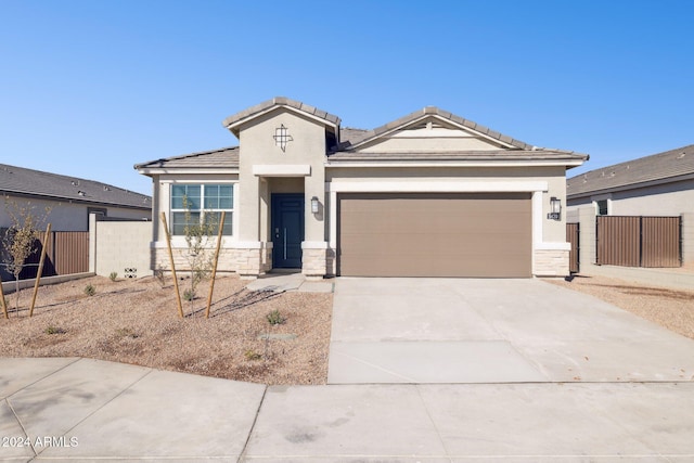 view of front of property with stucco siding, driveway, stone siding, fence, and an attached garage