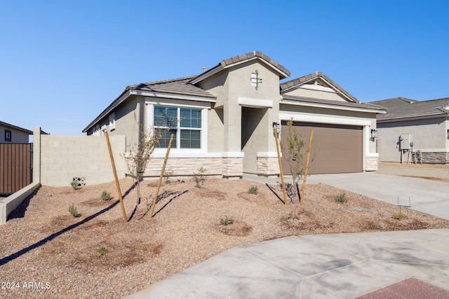 view of front of house with stucco siding, stone siding, fence, concrete driveway, and an attached garage