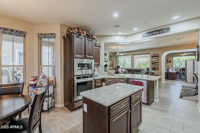 12738 W Brookhart Way, Peoria, AZ 85383 - kitchen with ceiling fan, appliances with stainless steel finishes, a peninsula, a kitchen island, and dark brown cabinetry