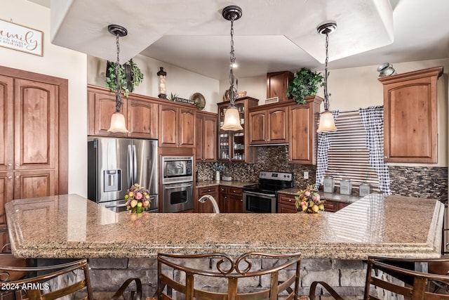 kitchen with appliances with stainless steel finishes, hanging light fixtures, a kitchen bar, decorative backsplash, and kitchen peninsula