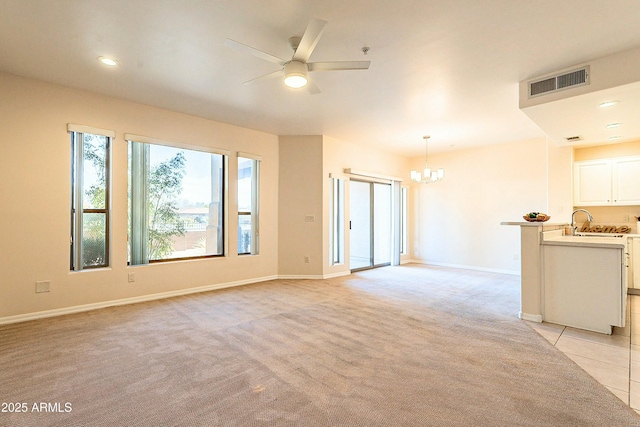 unfurnished living room featuring ceiling fan with notable chandelier, sink, and light colored carpet