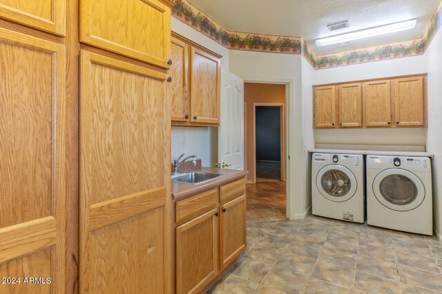 laundry room featuring washer and dryer, a textured ceiling, cabinets, and sink