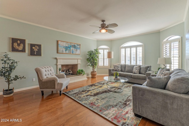 living room with a tiled fireplace, ceiling fan, crown molding, and hardwood / wood-style flooring