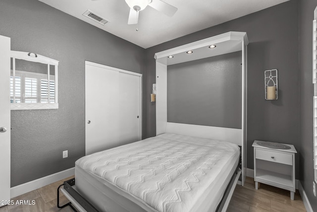 bedroom with visible vents, baseboards, a closet, wood finished floors, and a ceiling fan