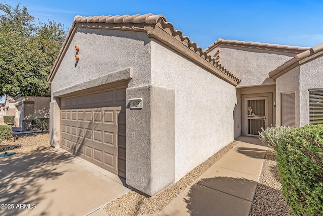view of side of property featuring stucco siding, a tiled roof, and an attached garage