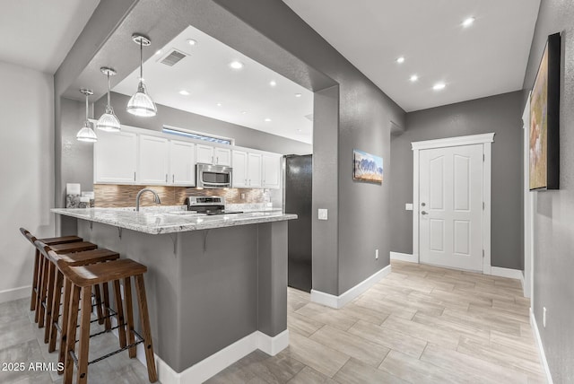 kitchen with a breakfast bar, stainless steel appliances, white cabinetry, visible vents, and a peninsula
