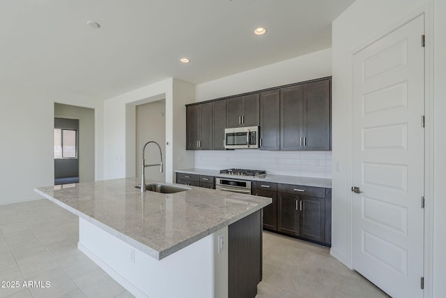 kitchen with sink, a center island with sink, light stone countertops, and appliances with stainless steel finishes