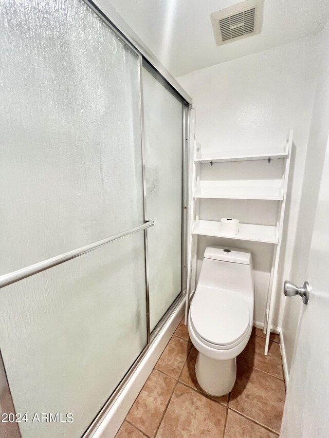 bathroom with a shower with shower door, tile patterned floors, and toilet