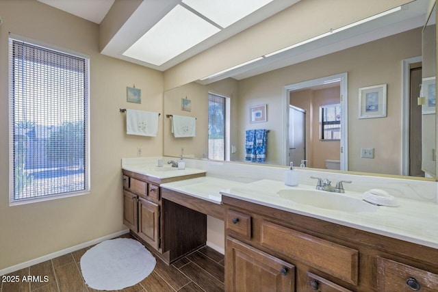 full bath featuring double vanity, a skylight, a sink, wood finish floors, and toilet