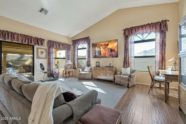 living area featuring vaulted ceiling, visible vents, wood finished floors, and a textured ceiling