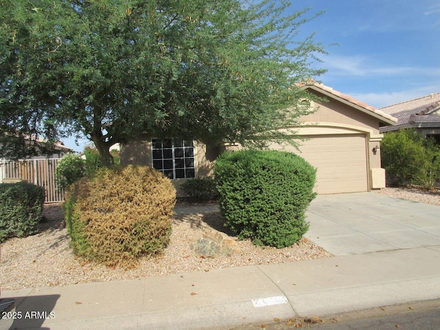 obstructed view of property with a garage, fence, driveway, a tiled roof, and stucco siding