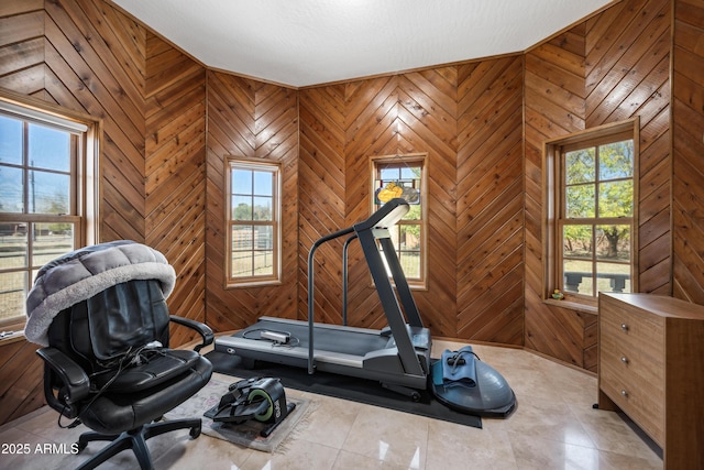 exercise area with a wealth of natural light, light tile patterned flooring, and wood walls