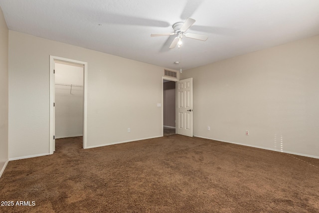 unfurnished bedroom featuring a walk in closet, visible vents, a ceiling fan, carpet flooring, and baseboards