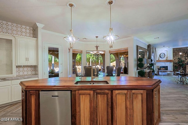 kitchen with stainless steel dishwasher, sink, decorative light fixtures, a fireplace, and a center island with sink