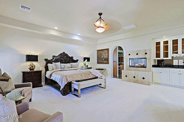 bedroom with light colored carpet and a tiled fireplace