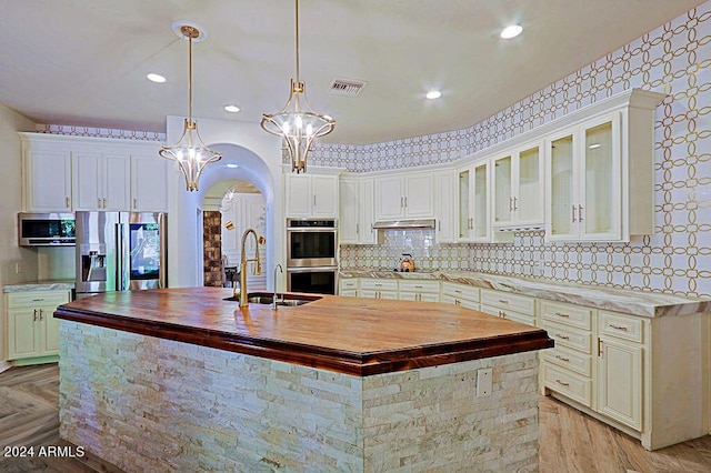 kitchen featuring a kitchen island with sink, butcher block counters, pendant lighting, and stainless steel appliances