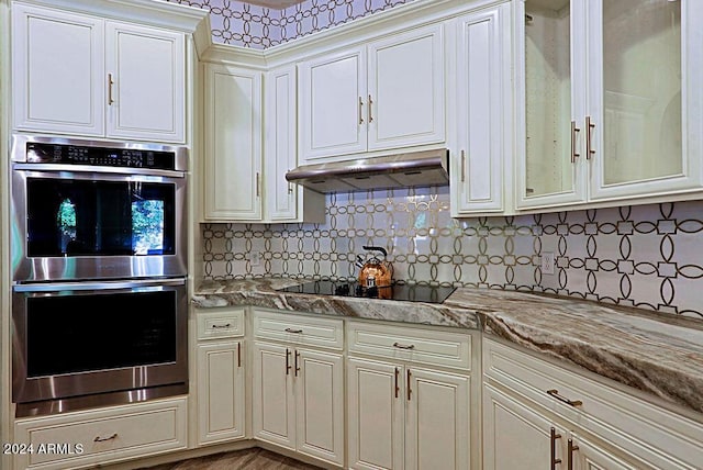 kitchen featuring black electric stovetop, double oven, tasteful backsplash, cream cabinets, and light stone counters