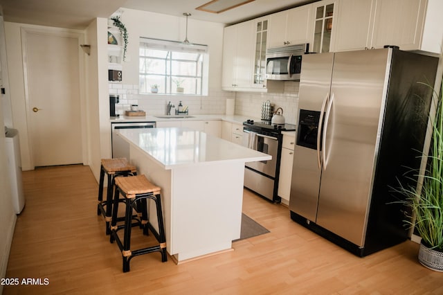 kitchen with white cabinetry, a kitchen island, stainless steel appliances, a kitchen bar, and decorative light fixtures