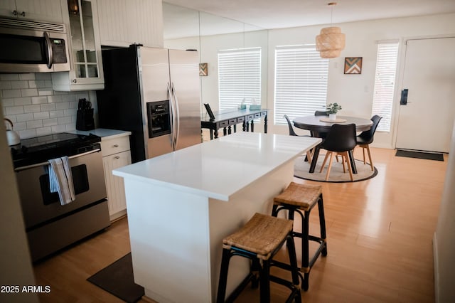 kitchen featuring light hardwood / wood-style flooring, decorative light fixtures, a breakfast bar area, and appliances with stainless steel finishes