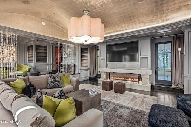 living room with built in features, lofted ceiling, wood finished floors, a lit fireplace, and a decorative wall