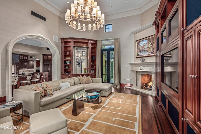 living area with arched walkways, dark wood-style flooring, crown molding, visible vents, and a lit fireplace