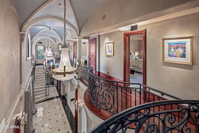 interior space with a chandelier, an upstairs landing, vaulted ceiling, and ornate columns