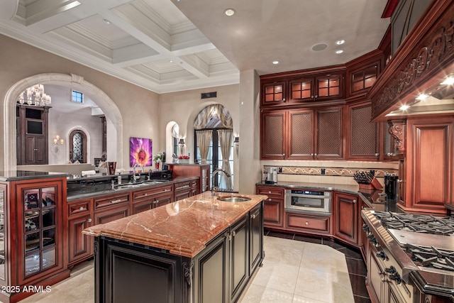 kitchen featuring an island with sink, dark stone countertops, a sink, and glass insert cabinets