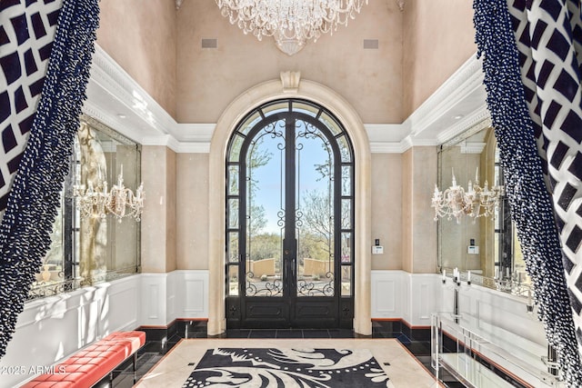 entrance foyer with arched walkways, a wainscoted wall, french doors, a chandelier, and a decorative wall