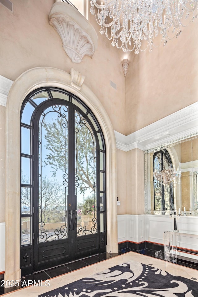 entrance foyer featuring a towering ceiling, tile patterned flooring, a chandelier, and french doors