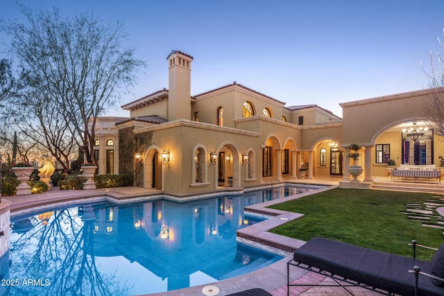 pool at dusk featuring a patio, a lawn, and an outdoor pool