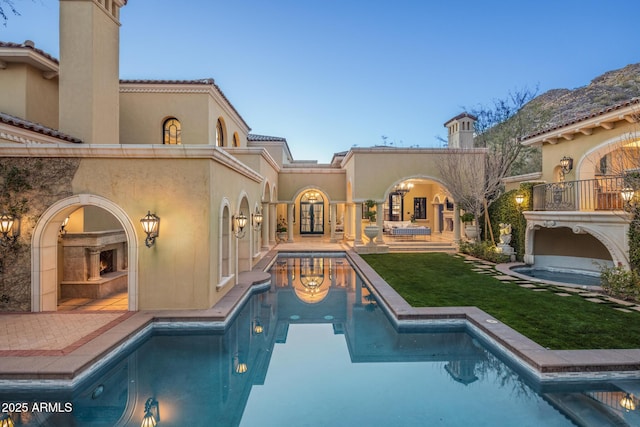 rear view of property with a patio area, an outdoor pool, a tiled fireplace, and stucco siding