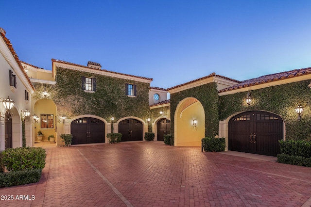 mediterranean / spanish-style house featuring driveway, a garage, a tile roof, a chimney, and stucco siding