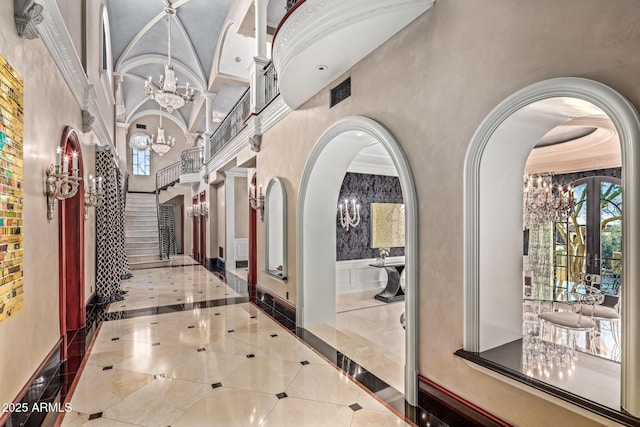 hallway featuring arched walkways, a towering ceiling, a wainscoted wall, a chandelier, and a decorative wall