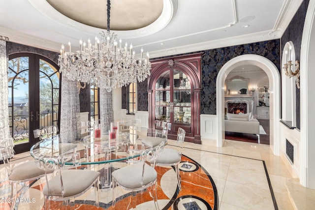 dining room with a large fireplace, arched walkways, a raised ceiling, crown molding, and french doors