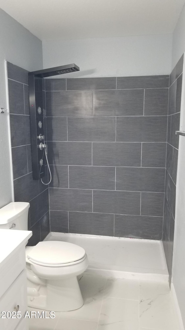 bathroom featuring toilet, vanity, marble look tile flooring, and a tile shower