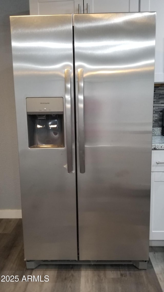 kitchen view of stainless steel fridge with ice dispenser, wood finished floors, white cabinetry, backsplash, and light stone counters