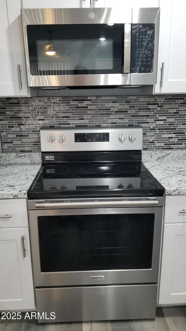 kitchen view of stainless steel appliances, white cabinetry, backsplash, and light stone countertops