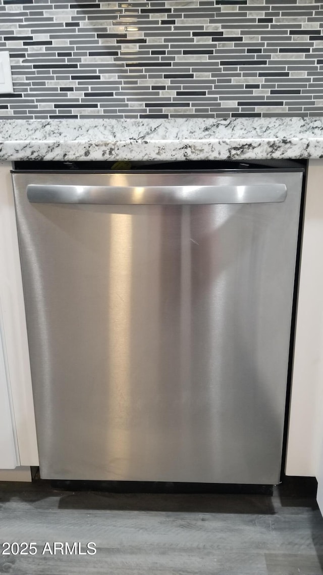 kitchen view of stainless steel dishwasher, tasteful backsplash, and light stone counters