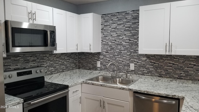 kitchen featuring stainless steel appliances, a sink, tasteful backsplash, white cabinets, and light stone countertops