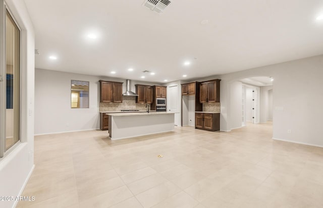 kitchen with recessed lighting, visible vents, wall chimney exhaust hood, decorative backsplash, and arched walkways