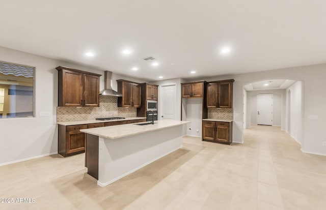 kitchen featuring tasteful backsplash, visible vents, arched walkways, a sink, and wall chimney range hood