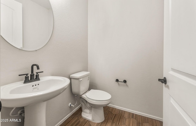 half bath with baseboards, a sink, toilet, and wood finished floors