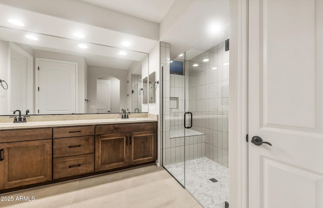 full bath with a stall shower, double vanity, a sink, and recessed lighting