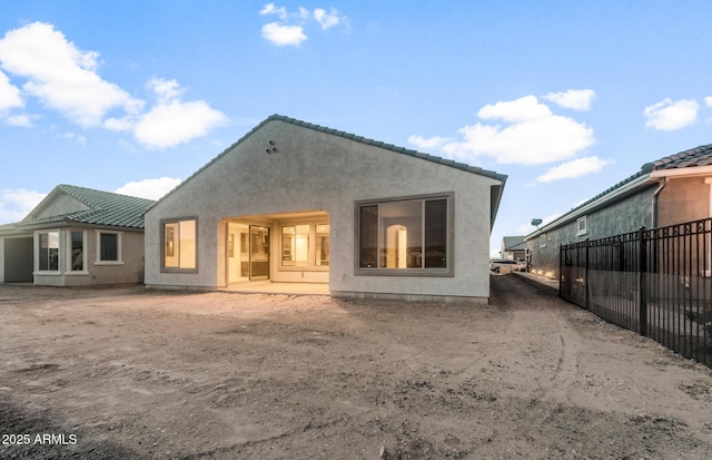 back of property with stucco siding, a tiled roof, and fence