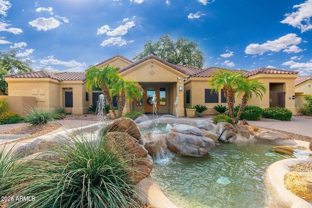 mediterranean / spanish house with a garden pond, stucco siding, and a tile roof