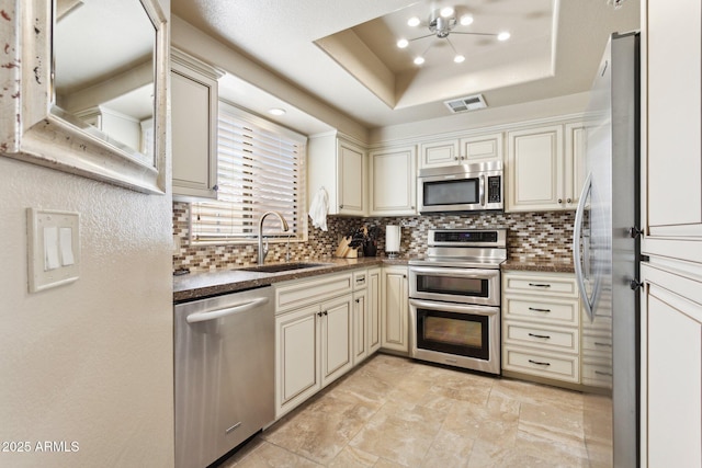 kitchen featuring appliances with stainless steel finishes, a sink, cream cabinets, backsplash, and recessed lighting