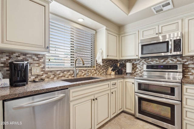 kitchen with cream cabinetry, appliances with stainless steel finishes, a sink, and decorative backsplash