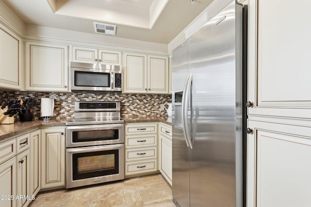 kitchen featuring appliances with stainless steel finishes, cream cabinets, a raised ceiling, and backsplash