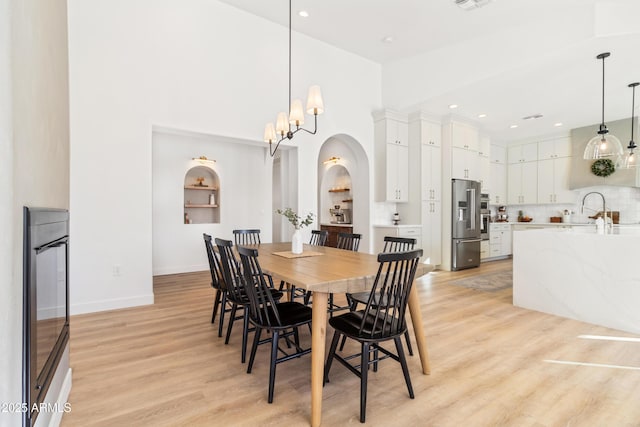 dining area with sink, a towering ceiling, a chandelier, and light hardwood / wood-style floors